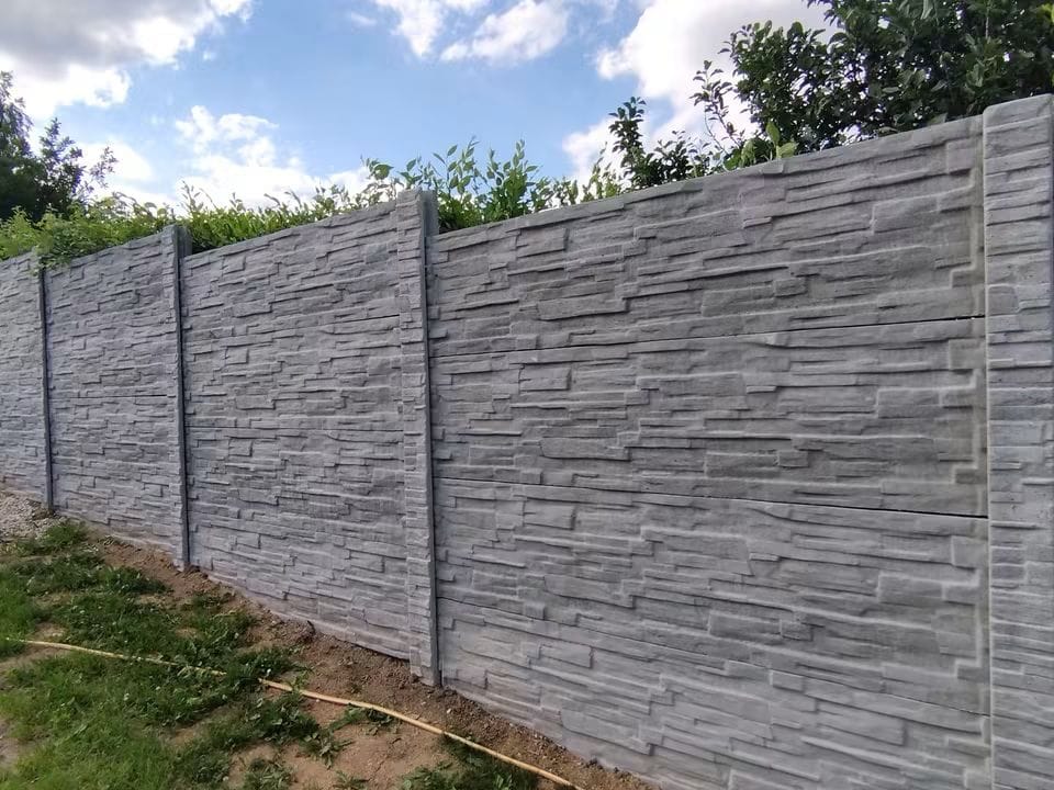 Dlouhý šedý betonový plot se vzorem skládaného kamene