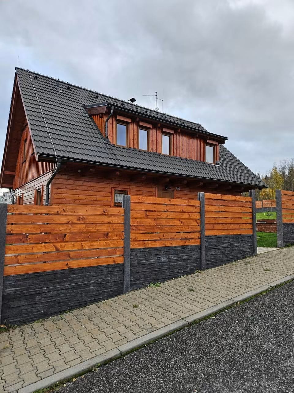 Antracitový betonový sokl kombinovaný s dřevěnými lamelami u roubeného domu