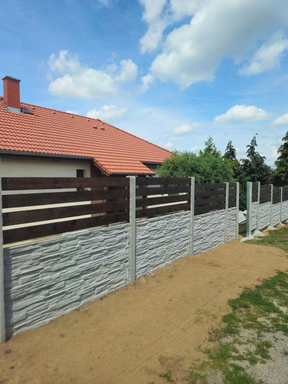 Světlý betonový plot kombinovaný s tmavě hnědou dřevěnou výplní