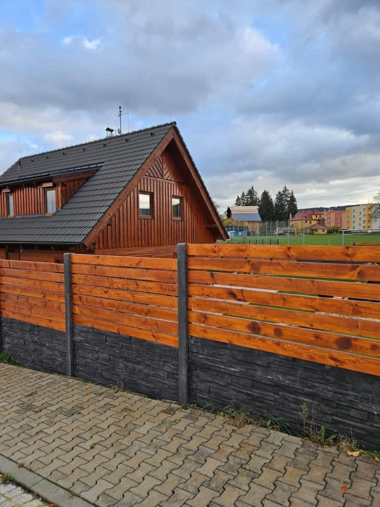 Antracitový betonový sokl s dřevěnou výplní podél chodníku